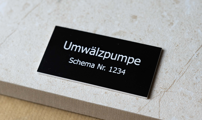 Schwarzes rechteckiges Kennzeichnungsschild mit weiß graviertem Text