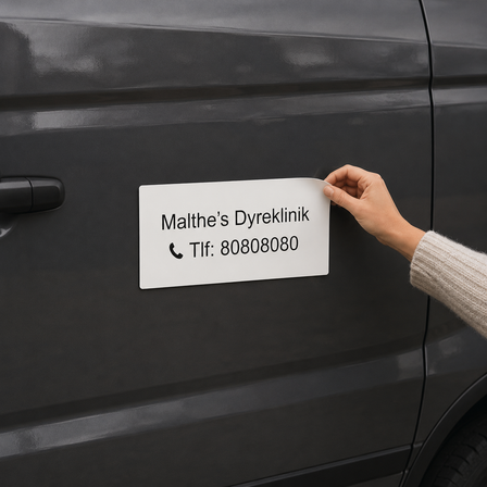 Hvid magnetskilt med teksten “Malthe’s Dyreklinik” og telefonnummer, monteret på siden af en mørkegrå varevogn