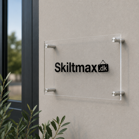 Klart akrylskilt med Skiltmax.dk-logo, monteret med sølvfarvede vægafstandsstykker på en lys facade i naturligt dagslys.