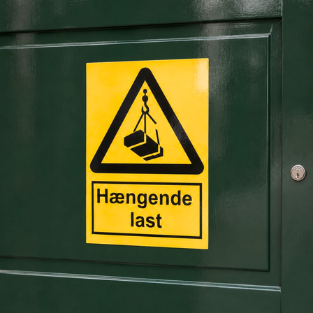 Gul, blank vinyldekal med advarselssymbolet “Hængende last”, monteret på en mørkegrøn, blanklakeret port.