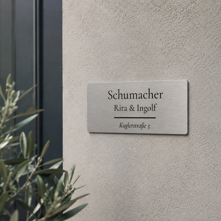 Bedrucktes Edelstahlschild mit der Aufschrift „Schumacher – Rita & Ingolf – Kuglerstraße 5“, an einer hellen Hausfassade neben dem Eingangsbereich angebracht.