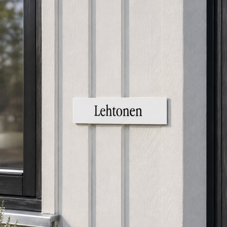 Valkoinen kaiverrettu muovinen nimikyltti mustalla pohjakerroksella ja tekstillä ”Lehtonen”, kiinnitettynä vaaleaan suomalaisen talon julkisivuun ulko-oven vieressä.